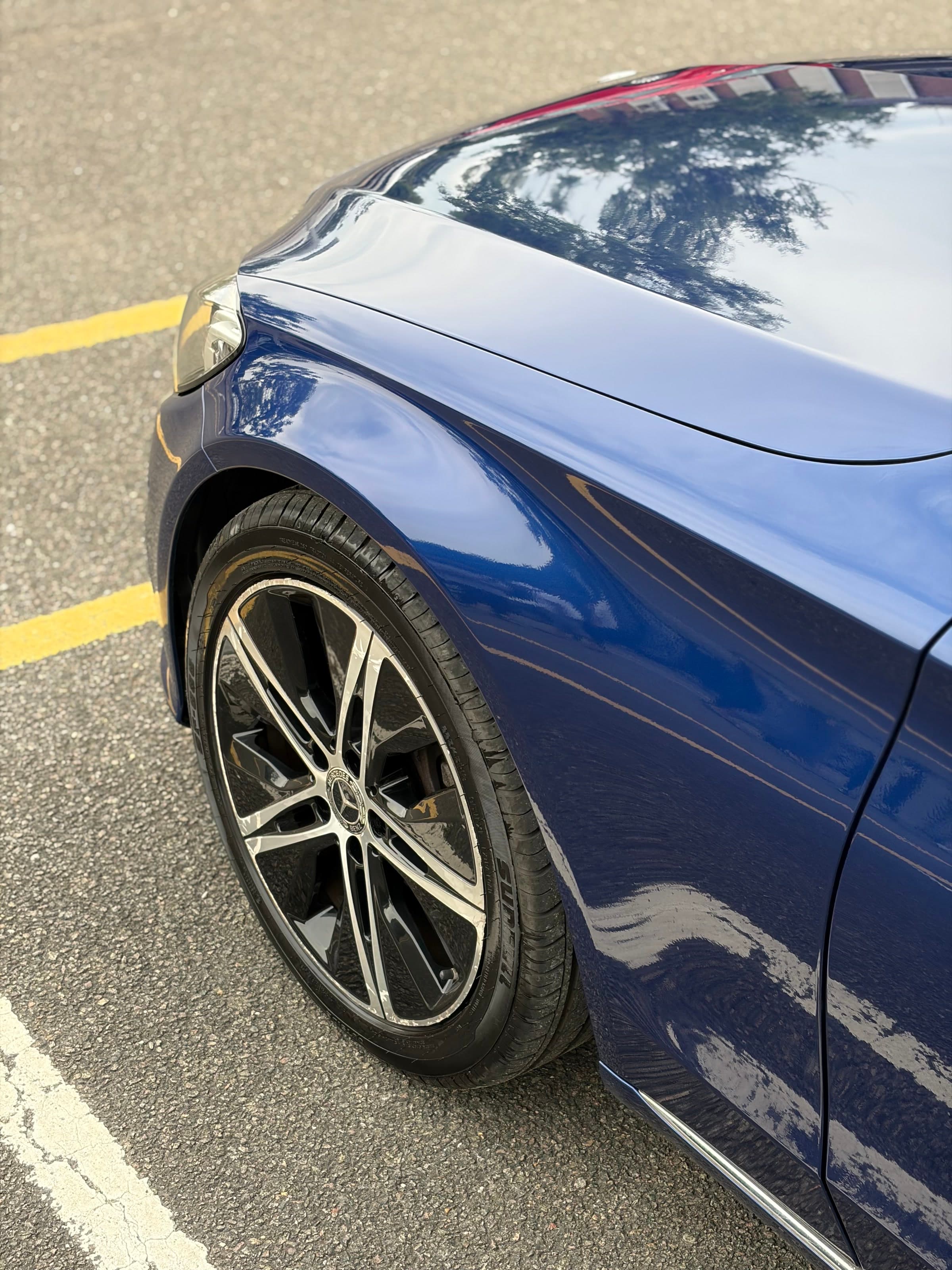 Front wing of a blue Mercedes C-Class reflecting the trees above it